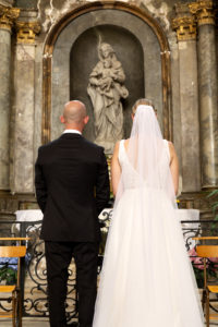 Photographie de deux mariés devant une statue de Marie dans une église